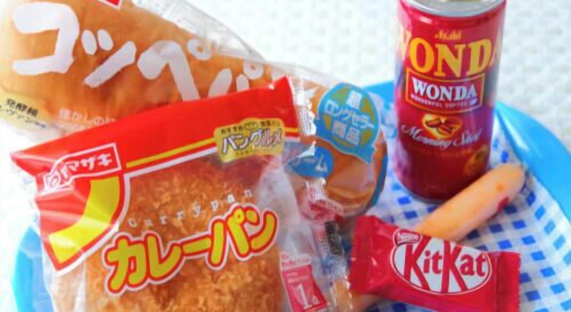 A snack tray with a bag of rice crackers, a can of Wonda soda, a KitKat bar, and a baguette.