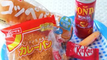 A snack tray with a bag of rice crackers, a can of Wonda soda, a KitKat bar, and a baguette.