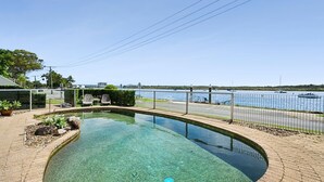 A clear swimming pool with a view of the water and boats, surrounded by a paved deck and a metal fence. - sunny, north-facing ground-floor apartment (Noosaville)