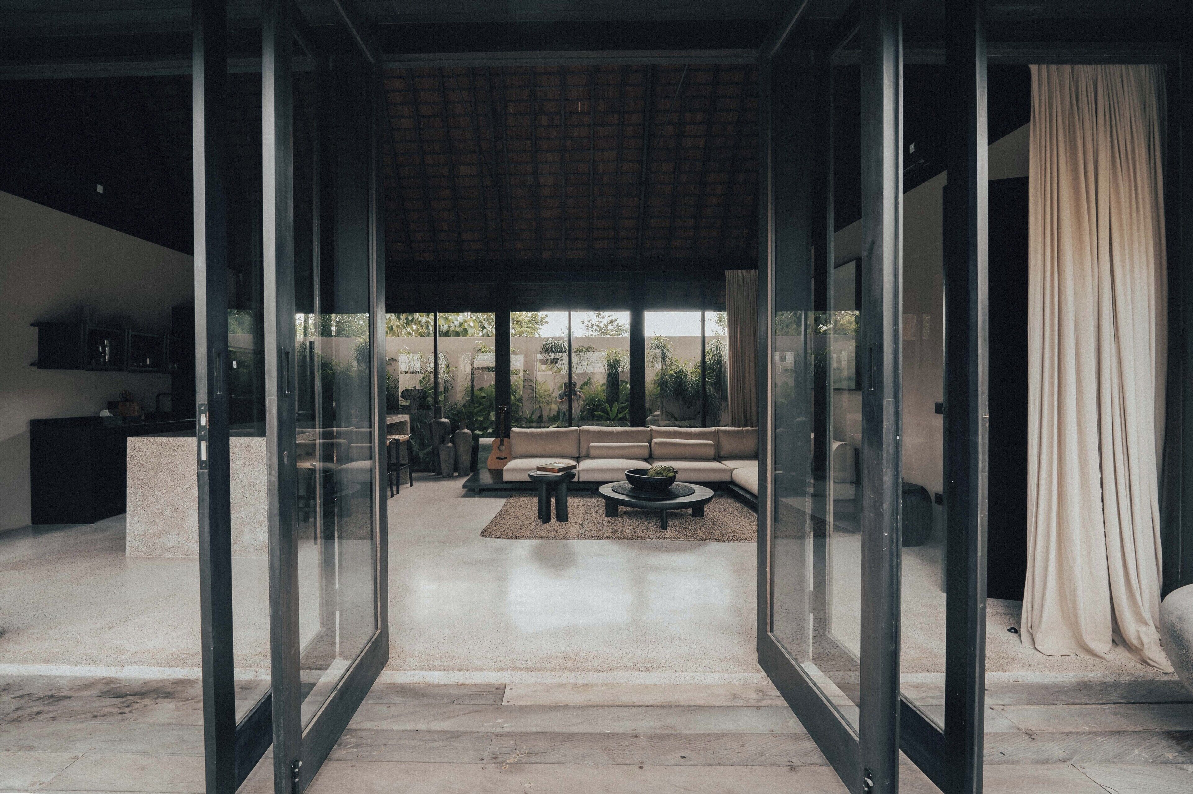 Un interior moderno con un vidrio que da a un área de estar que incluye un sofá, una mesa de centro y vistas al exterior.