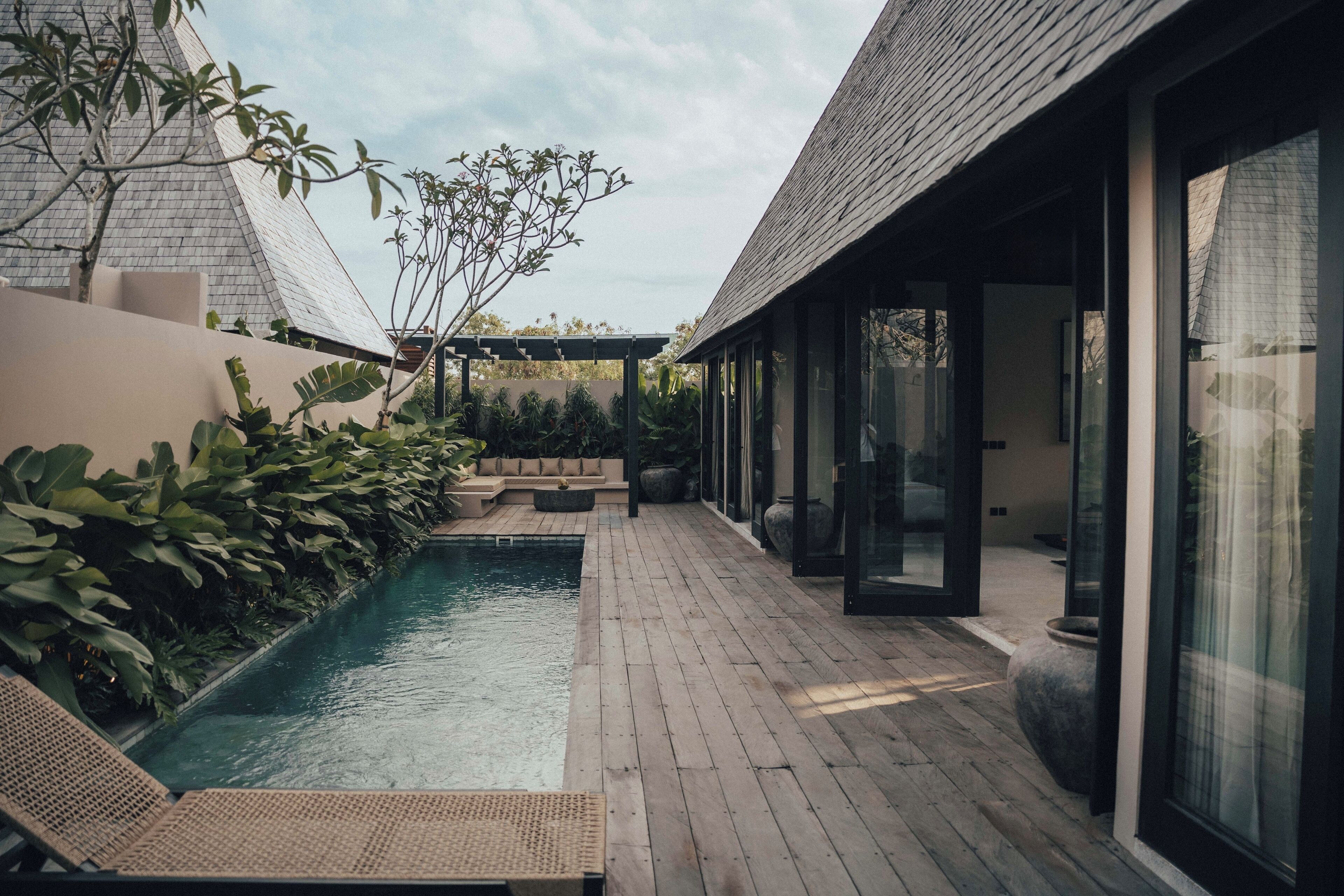 A modern outdoor pool area with wooden decking, lounge chairs, and a pergola.