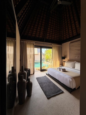 A hotel room with a bed, a large window with curtains, a view of a pool, and several vases.