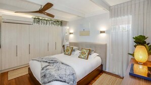 Quarto com cama, ventoinha no teto, mesa de cabeceira com abajur e janela com cortinas.