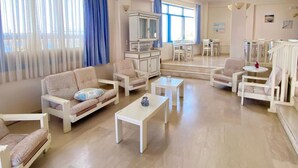 A spacious living room with a large window, a dining area, and a kitchen in the background. - Pallada Apartment (Agios Vasileios)