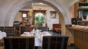 A dining area with a stone archway, tables set with white tablecloths, and a kitchen area with a coffee machine and utensils. - Hotel Ionas (Chania)