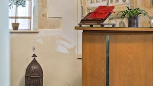 A room with a wooden desk, a potted plant, a decorative lantern, and a mural of a building on the wall. - Hotel Ionas (Chania)