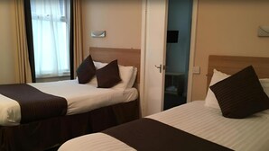 Deux lits simples avec des têtes de lit marron et du linge de lit blanc, dans une chambre d’hôtel.
