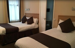 Två separata sängar med bruna sänggavlar och vitt sänglinne i ett hotellrum.
