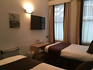 Ett hotellrum med två sängar, ett skrivbord, en TV och ett fönster med gardiner.