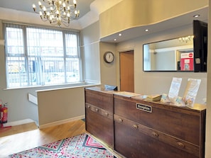 A reception desk with a clock, a window with blinds, a chandelier, and a mirror. - Lord Nelson Hotel (Liverpool)