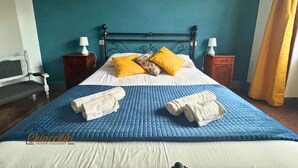 Una cama con un edredón azul, dos almohadas amarillas y dos toallas enrolladas.