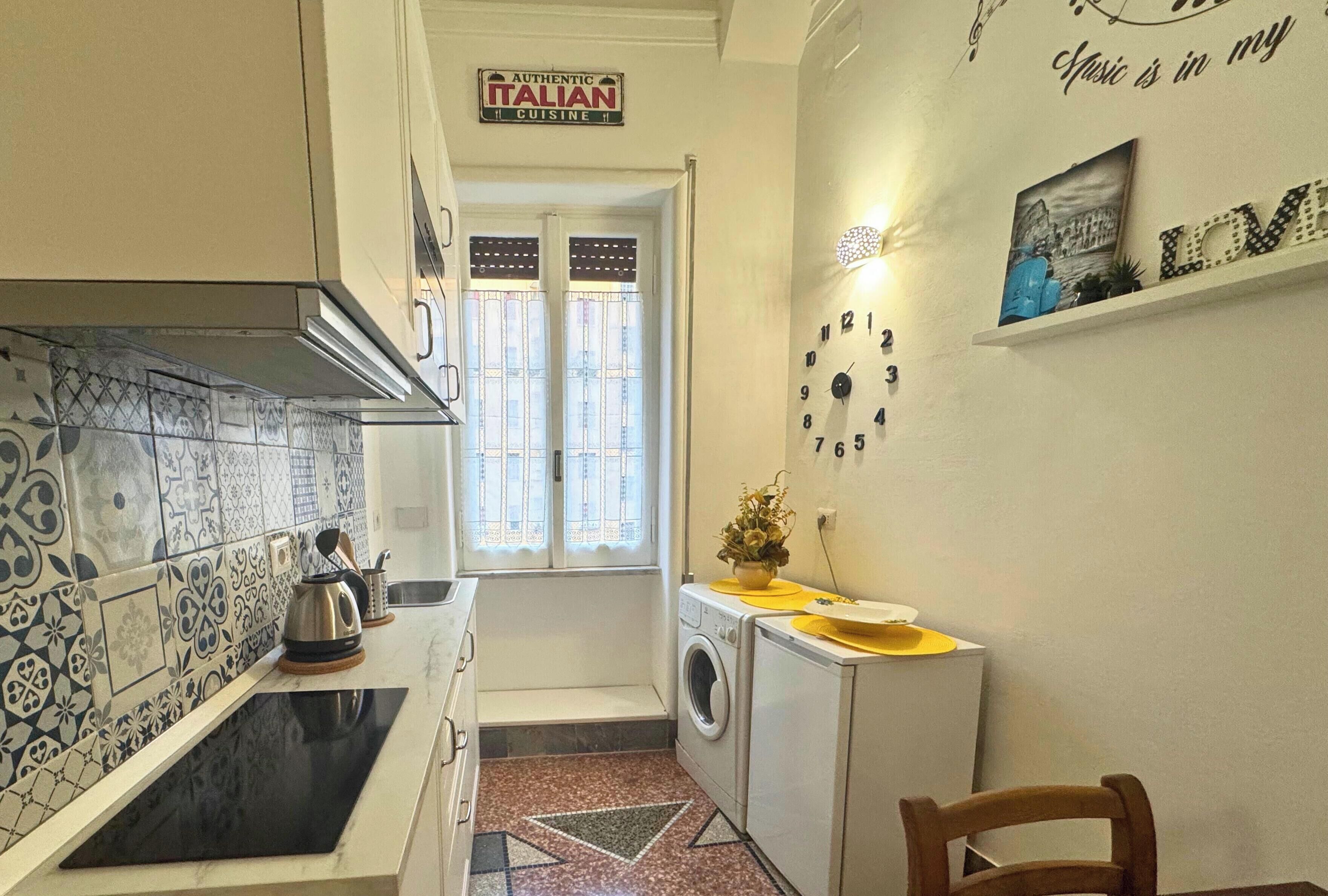 A compact kitchen with a washing machine, a sink, and a window with decorative curtains.