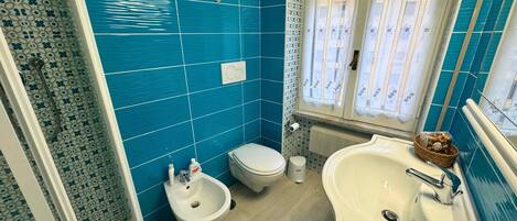 Un baño con azulejos azules, un lavabo blanco, un bidé y un inodoro.