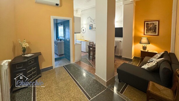Un hall de hotel con un sofá negro, una mesita con lámpara, un espejo y un jarrón decorativo.