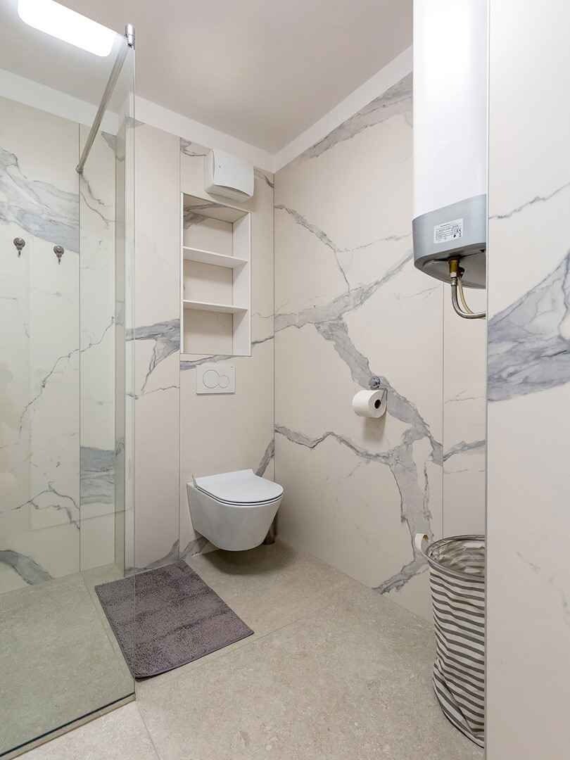 A bathroom with a shower, toilet, and marble walls.