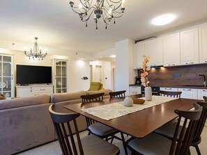 A modern living room with a sofa, dining table, and chairs, a TV, and a kitchen area with cabinets and a countertop. - Holiday apartment with cosy furnishings and large loggia (Poreč)