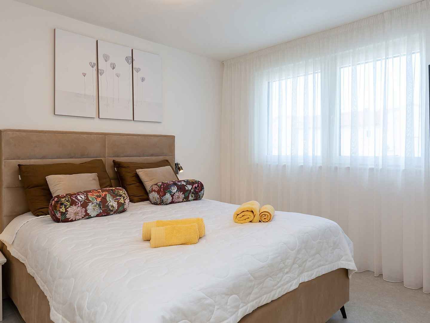 A neatly made bed with a white duvet, two floral pillows, and two rolled towels.