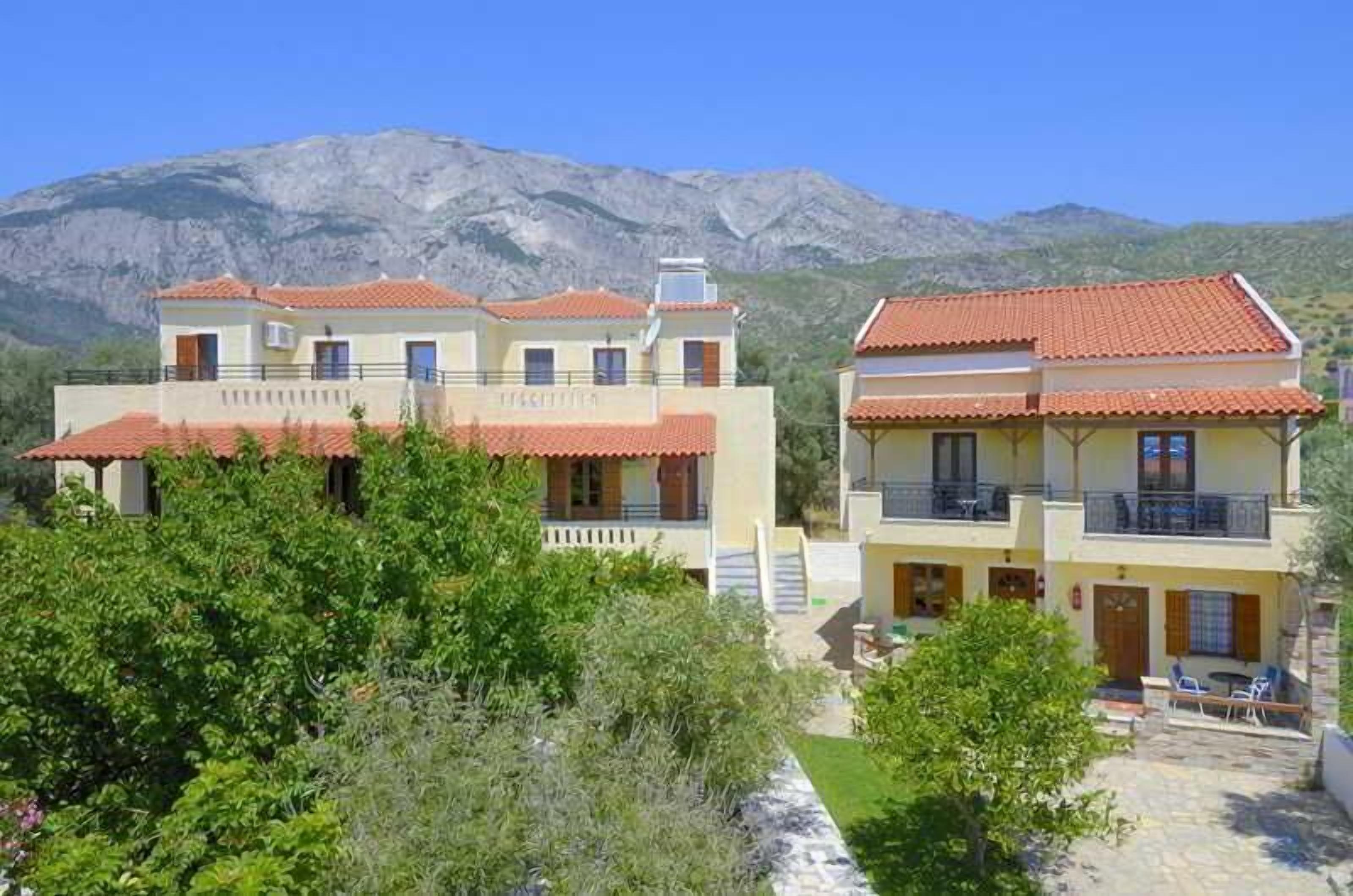 A two-story building with a red-tiled roof, balconies, and a mountainous backdrop.