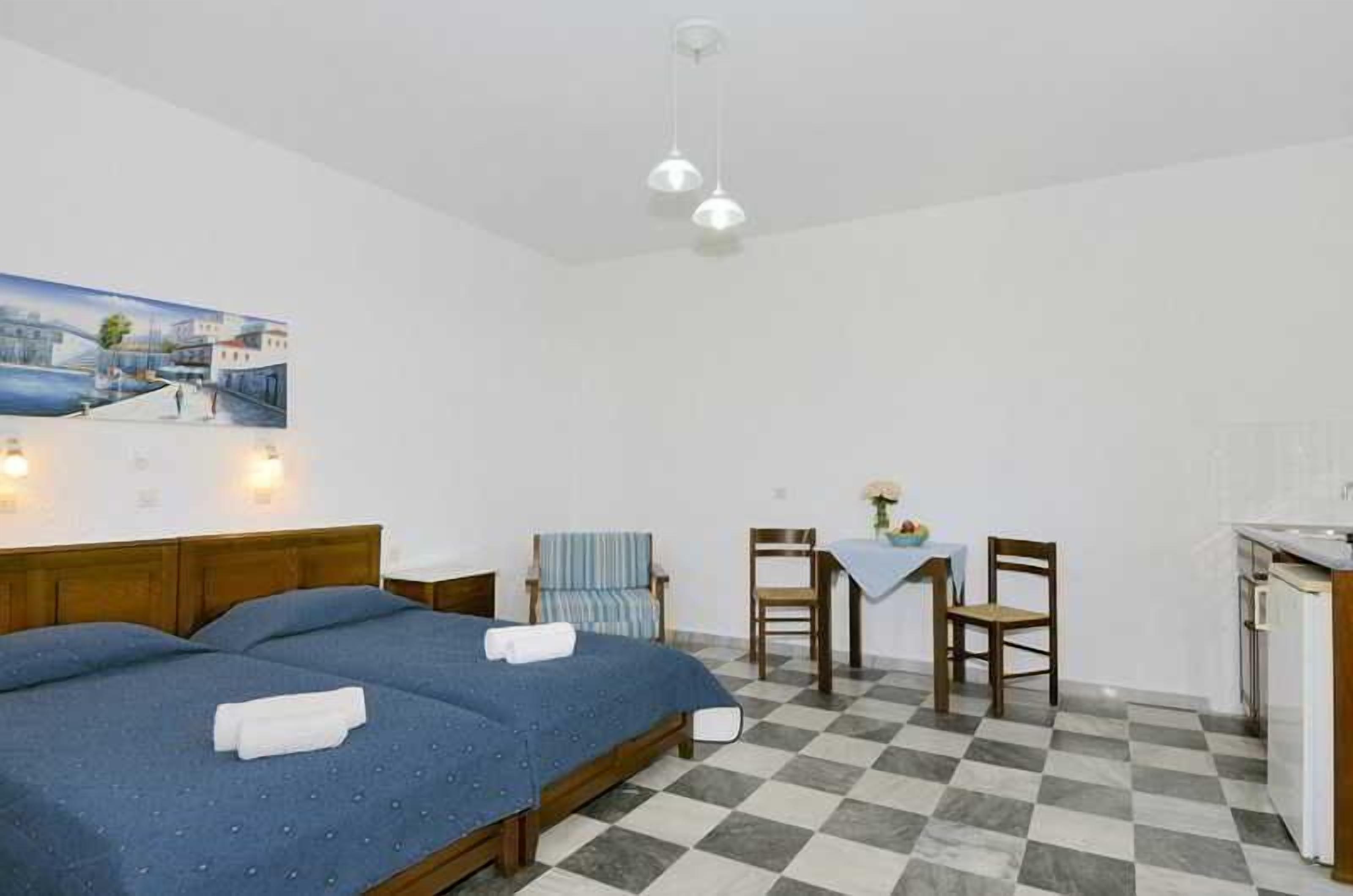 A room with a bed, two chairs, a small table, and a kitchenette.