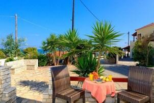 Un patio al aire libre con sillas de mimbre, una mesa con mantel rosa y una cesta de frutas.