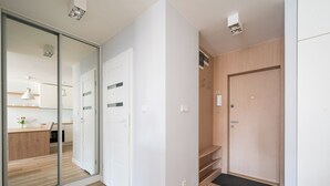 Ein modernes Interieur mit Holzboden, weißen Wänden, einer Schiebeglasdoor zu einer Küche und einer Holztür mit einer kleinen Ablagefläche.