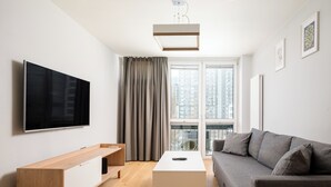 Ein modernes Wohnzimmer mit einem Flachbildfernseher, einem Holztischelement, einem weißen Couchtisch und einem grauen Sofa.