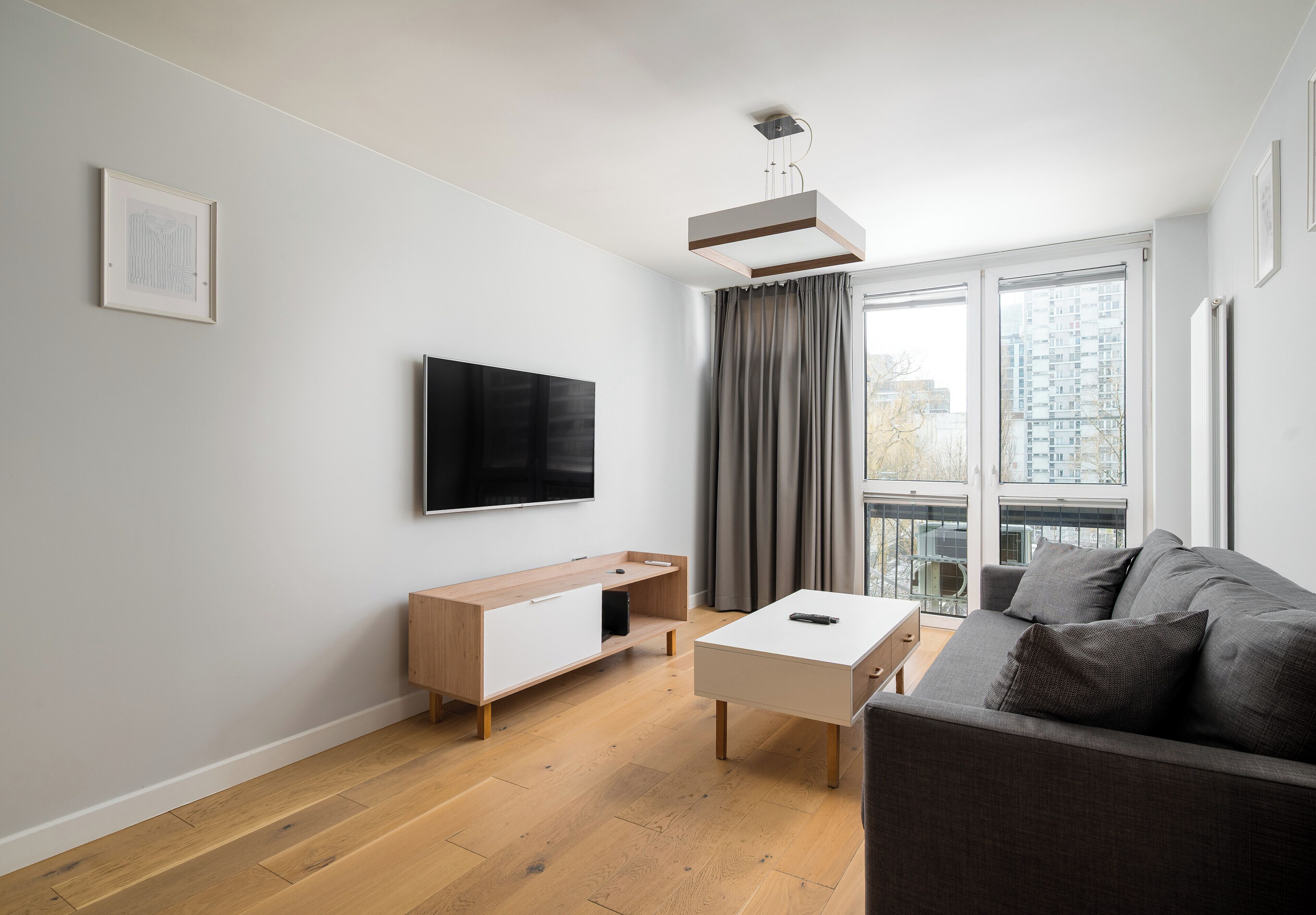 Un salon moderne avec un tél éviseur à écran plat, un meuble en bois, une table basse blanche et un canapé gris.