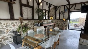 Un comedor con una mesa de vidrio y sillas blancas, rodeado de paredes de piedra y vigas de madera.