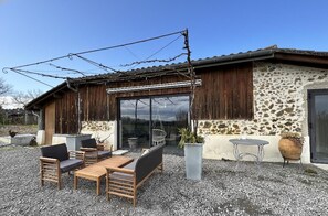 A rustic building with a stone exterior, wooden shutters, and a gravel patio with outdoor furniture. - Lou Sarrat - MIMBASTE (MIMBASTE)