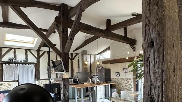 Amplia sala de estar con vigas de madera a la vista, una mesa de comedor de cristal y una cocina moderna al fondo.