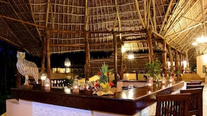 An outdoor bar area with a thatched roof, wooden bar counter, and seating. - Ocean Paradise Resort Zanzibar (Kiwengwa)