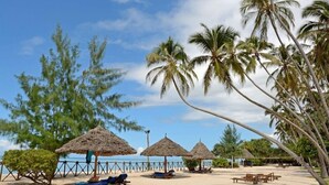 A beach with thatched umbrellas, lounge chairs, and palm trees. - Ocean Paradise Resort Zanzibar (Kiwengwa)