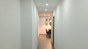 A narrow hallway with white walls and dark grey tiled flooring. There are recessed ceiling lights and a door at the end of the hallway. - Exclusive location, close to the Mall and main attraction. (San Salvador)