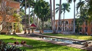 A pool area with a water feature, palm trees, and a building with arches. - Hacienda Uxmal (Santa Elena)