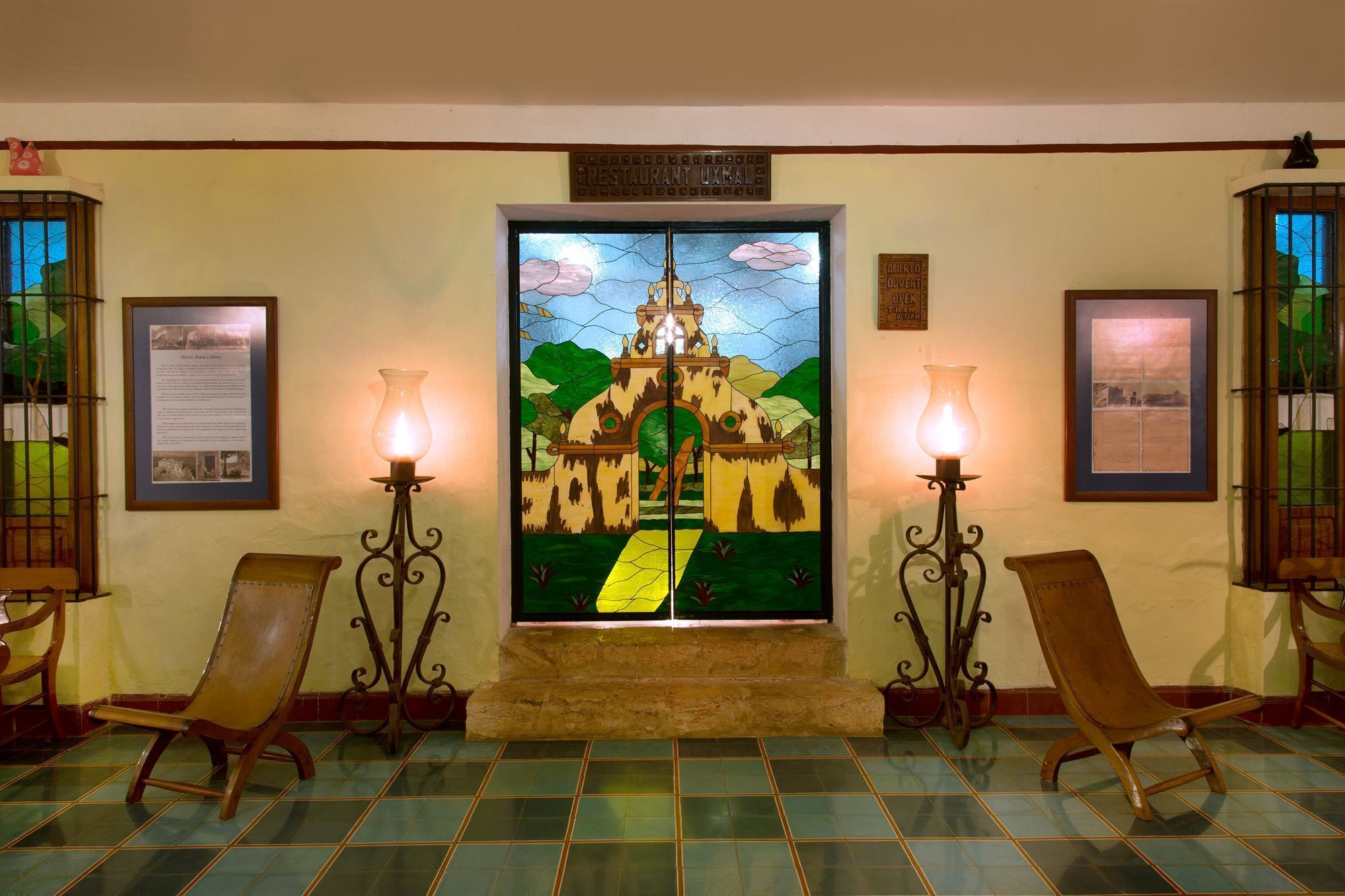 Un vestíbulo con un vitral que representa un castillo, dos sillas de madera y dos lámparas de pared.