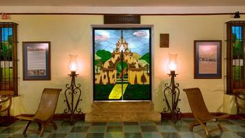 Un vestíbulo con un vitral que representa un castillo, dos sillas de madera y dos lámparas de pared.