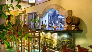 A bar area with wooden chairs, a bar counter, and decorative elements including a mural and a wooden barrel. - Hacienda Uxmal (Santa Elena)