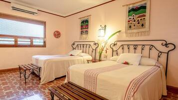 Una habitación de hotel con dos camas individuales, un banco, una ventana con persianas y obras de arte en las paredes.