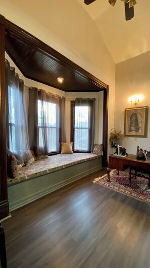 A room with a bay window seating area, a wooden bench, a rug, and a framed picture on the wall.