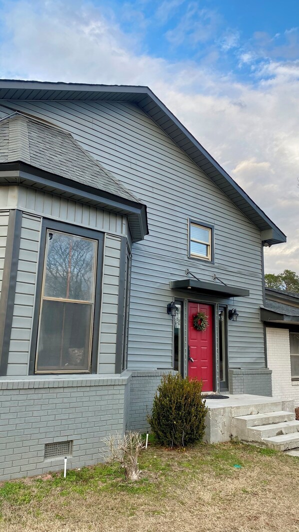A two-story house with a red door, a small porch, and a brick foundation.