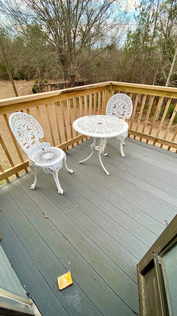 A wooden deck with two ornate white metal chairs and a table.