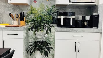 Une cuisine avec des meubles blancs, un four à micro-ondes, une machine à café et une plante en pot.