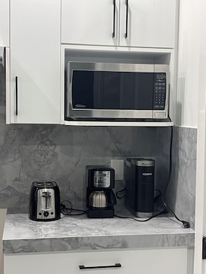 A kitchen with a built-in microwave, a coffee maker, and a toaster on a marble countertop. - Modern Delta Stay Near Vancouver + Parking (Delta)