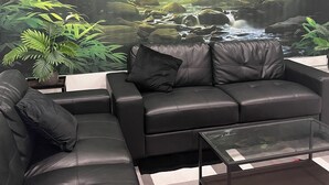 A modern living room with a black leather sofa, a glass coffee table, and a large wall mural of a jungle scene. - 5-Star 1BR Suite | Free Parking & Fast Wi-Fi (Delta)