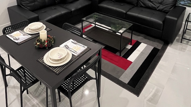 A modern living room with a black leather sectional sofa, a glass coffee table, and a dining table set for two. A large wall mural depicts a lush forest scene. - 5-Star 1BR Suite | Free Parking & Fast Wi-Fi (Delta)