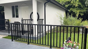 A house with a white exterior, black railing, and a flower pot on the porch. - 5-Star 1BR Suite | Free Parking & Fast Wi-Fi (Delta)