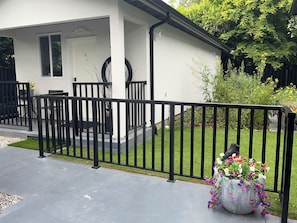 Una casa con facciata bianca, recinzione in metallo nero, vialetto in cemento e un vaso fiorito con diversi fiori.