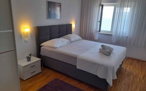 Ein Schlafzimmer mit einem Bett, Nachttischlampen, einem Nachttisch, einem Fenster mit Vorhängen und Blick ins Freie.