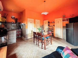 Une cuisine compacte avec un coin repas, comprenant une table et des chaises en bois, un réfrigérateur et un luminaire suspendu.