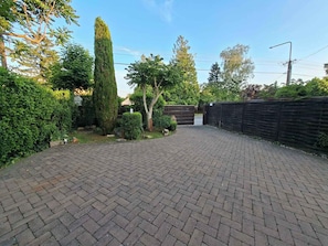 A paved courtyard with a brick pattern, surrounded by greenery and a wooden fence.